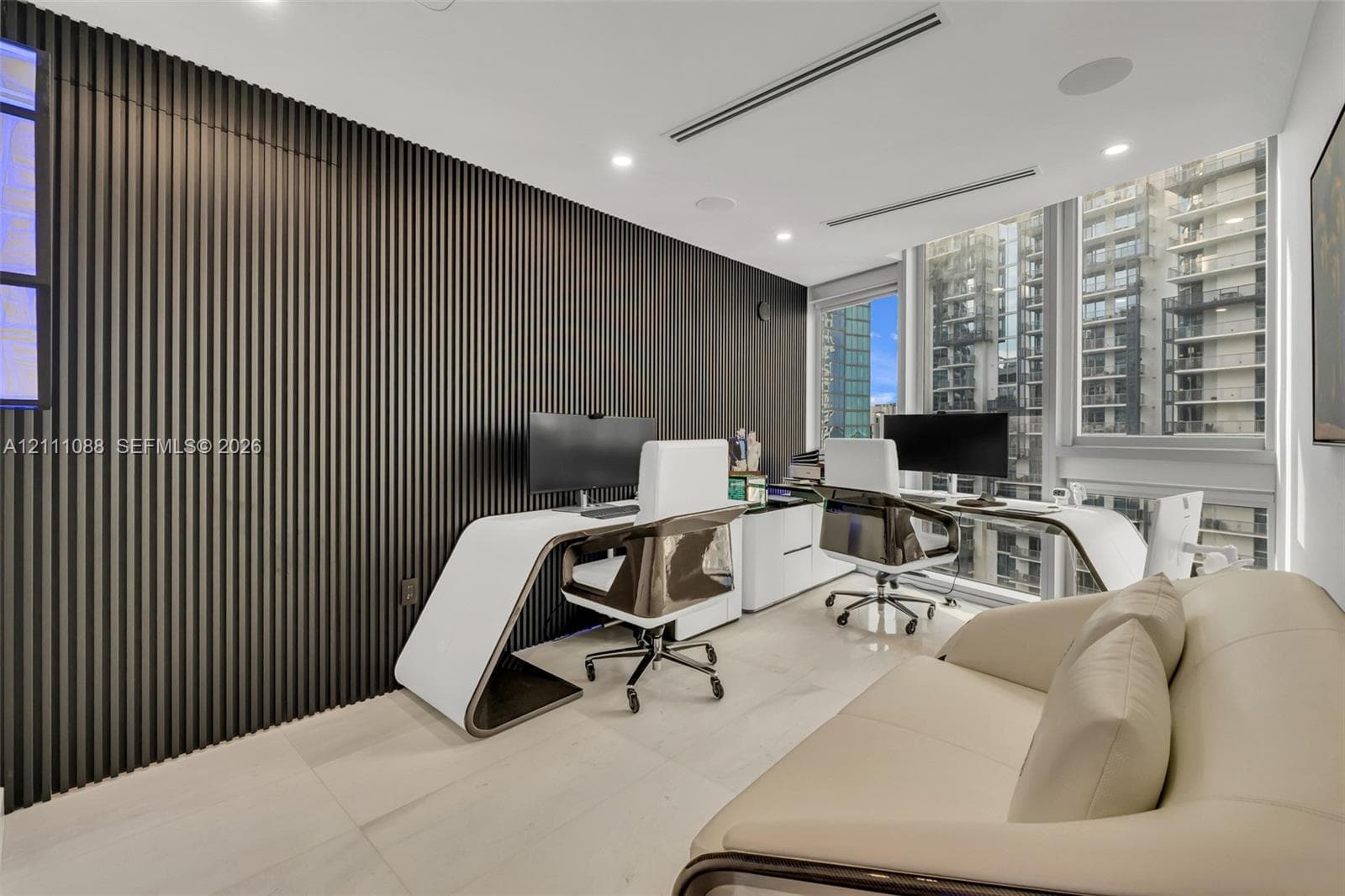 Interior space featuring a full-height, dark-toned slat wall treatment, neutral-toned large-format flooring, recessed ceiling lighting, integrated audio speakers, and expansive floor-to-ceiling windows