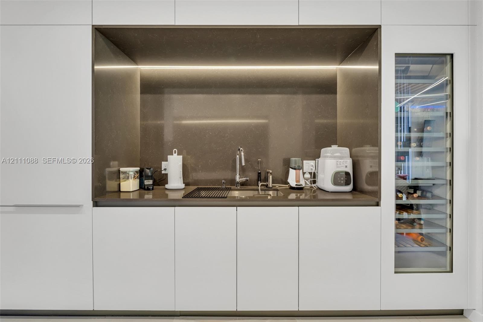 Minimalist built-in cabinetry featuring sleek matte white paneling, stone-finish countertops, integrated beverage refrigeration, and concealed LED task lighting