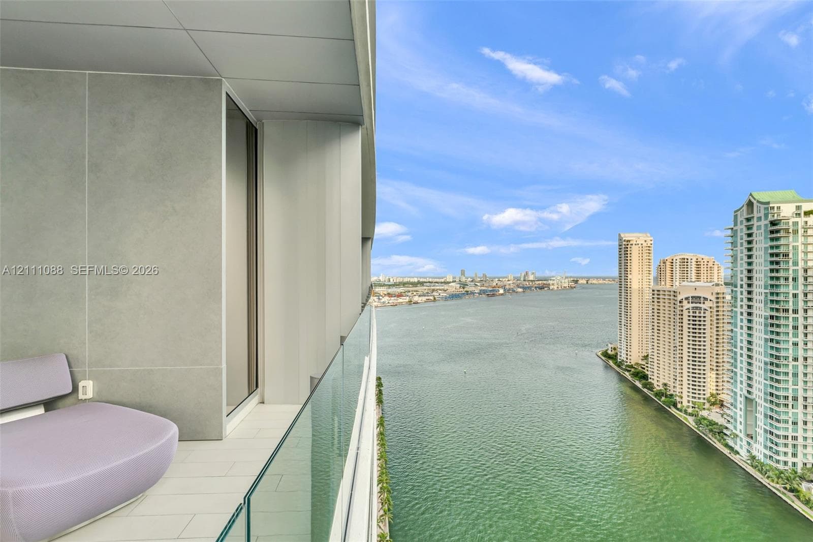 Private balcony featuring large-format tile flooring, concrete-finish wall panels, and a frameless glass railing overlooking the waterway