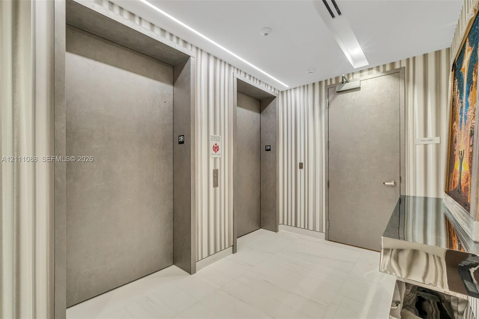 Elevator foyer featuring dual elevator doors with matte grey finish, full-height striped wall coverings, recessed ceiling lighting, and large-format tile flooring