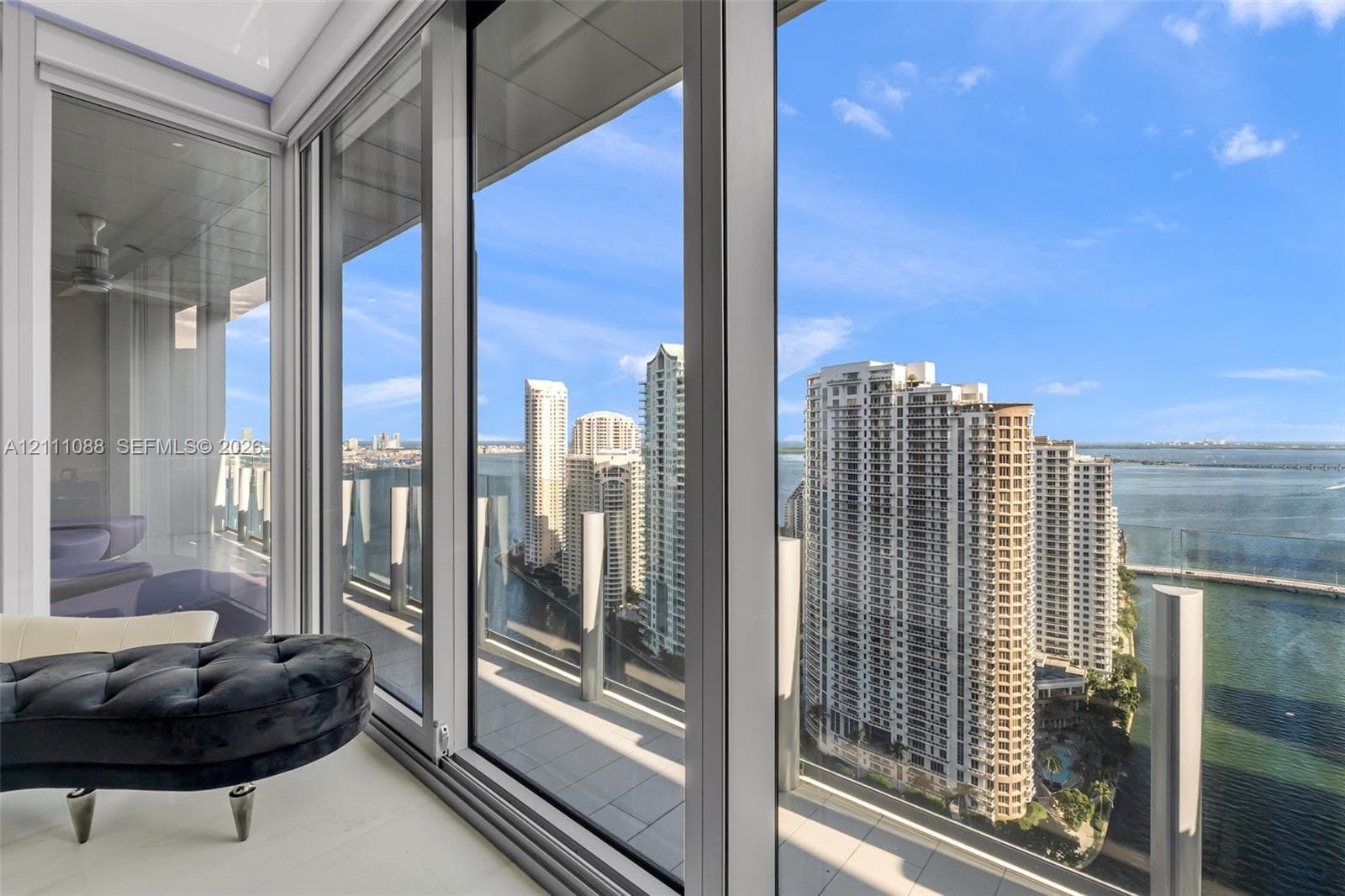 Floor-to-ceiling glass paneling, metal-frame sliding doors, expansive balcony featuring a glass balustrade, and high-rise cityscape and water scenery