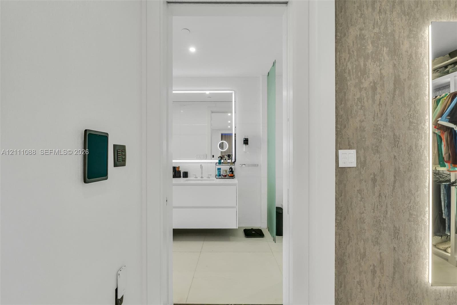 Floating white vanity with integrated lighting, oversized backlit mirror, large-format tile flooring, textured wall finish, and full-length edge-lit mirror panel