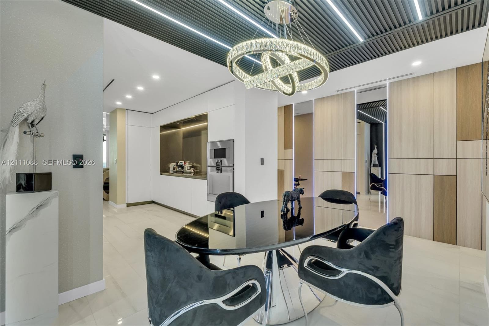 Slatted ceiling with integrated linear lighting, custom circular crystal chandelier, built-in floor-to-ceiling cabinetry with wood-finish paneling, and smooth-surface flooring