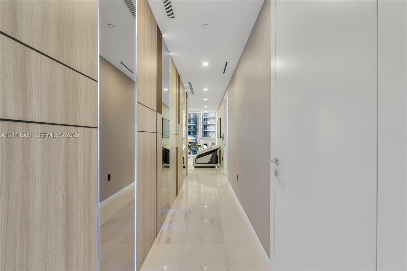 Hallway featuring floor-to-ceiling wood-finish wall paneling, full-length mirror accents, polished tile flooring, and recessed ceiling lighting