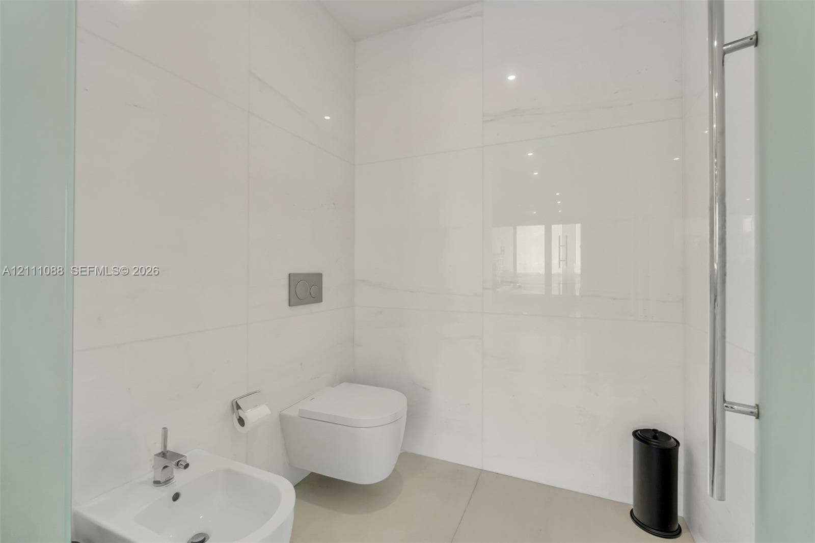 Wall-to-wall large-format porcelain tile, wall-mounted dual-flush toilet, pedestal bidet with chrome fixtures, and a vertical chrome towel warmer