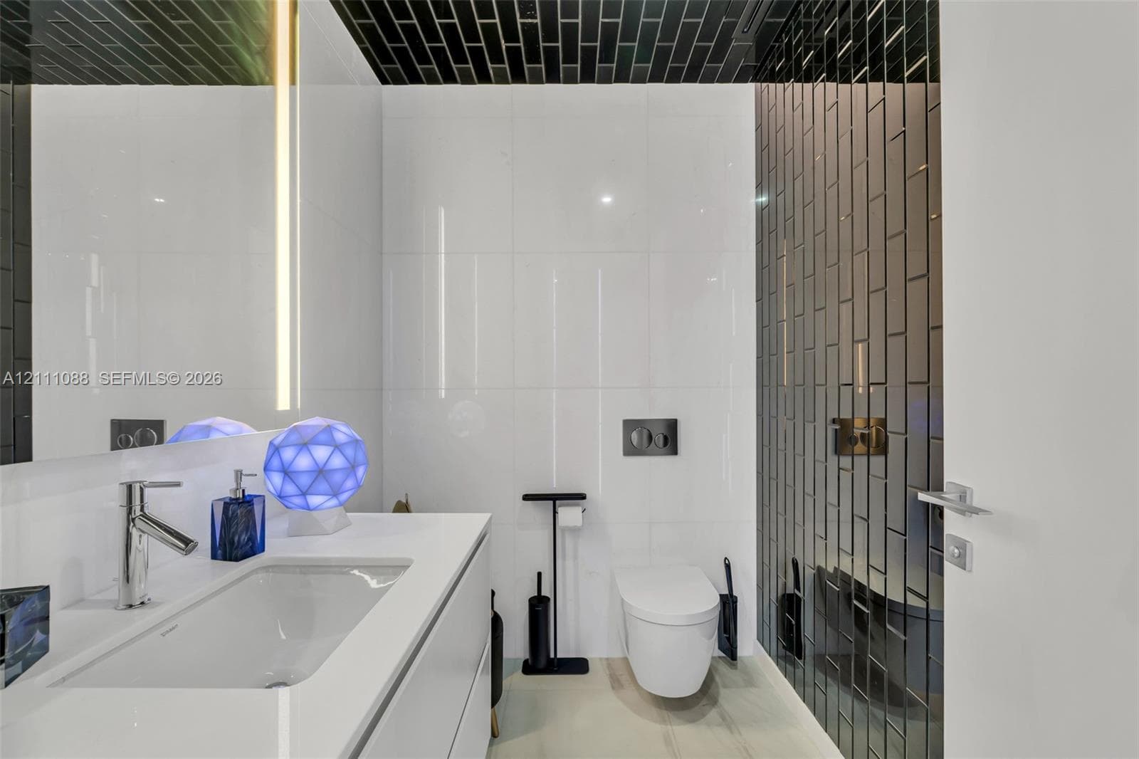 Modern vanity with a seamless integrated sink and countertop, wall-mounted toilet, floor-to-ceiling white wall tile, and black vertical glass subway tile accent walls