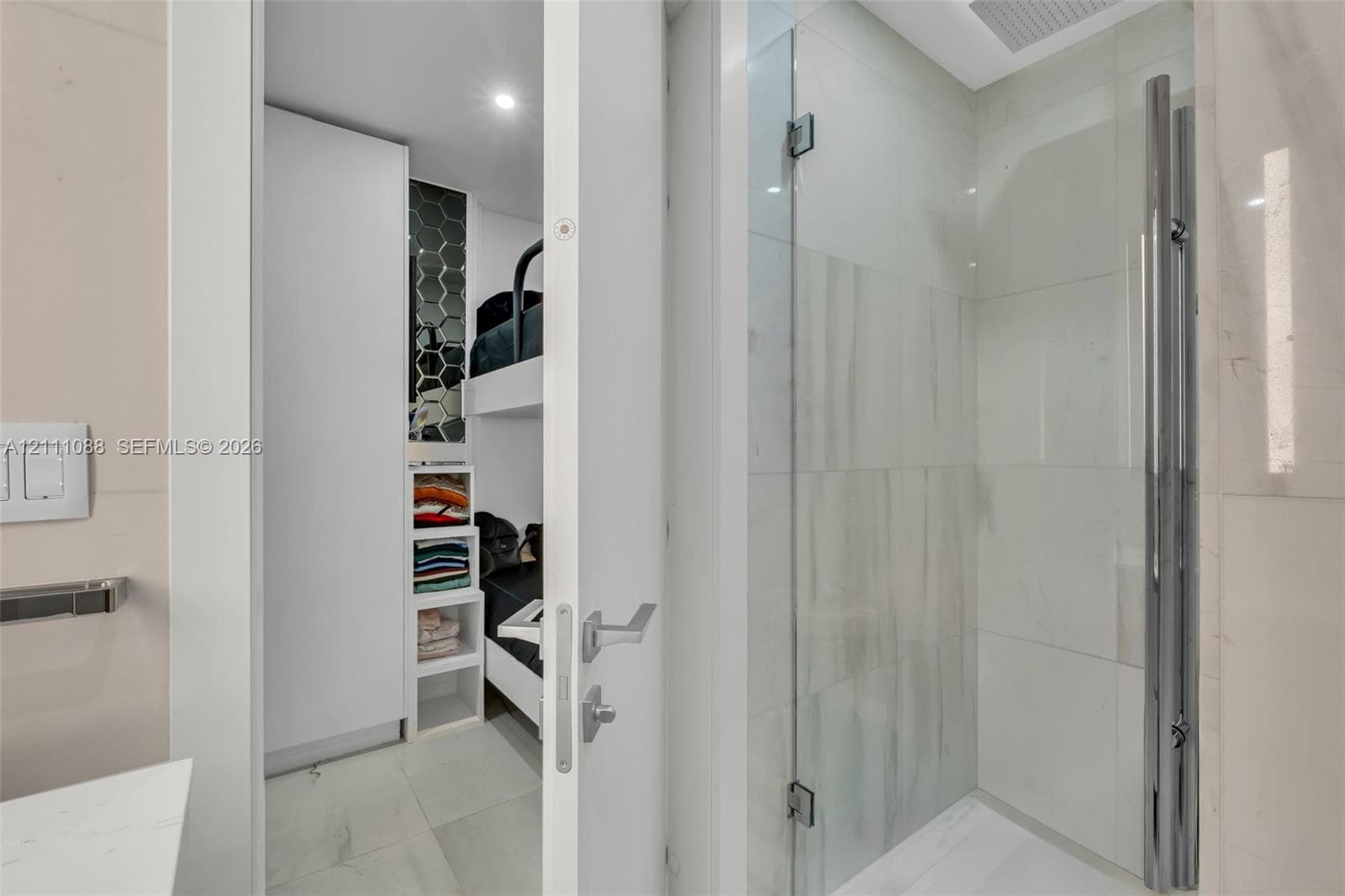 Shower enclosure featuring a seamless glass door, large-format polished wall tiling, and a vertical chrome hardware fixture