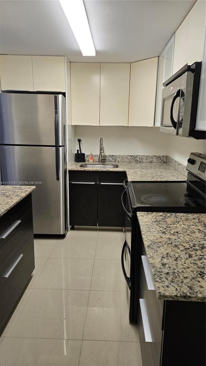 Kitchen featuring stainless steel appliances, speckled stone countertops, dual-tone cabinetry, and light-toned tile flooring