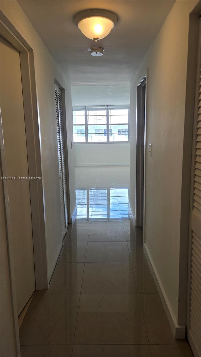 Hallway featuring large-format tile flooring, louvered closet doors, and flush-mount ceiling lighting