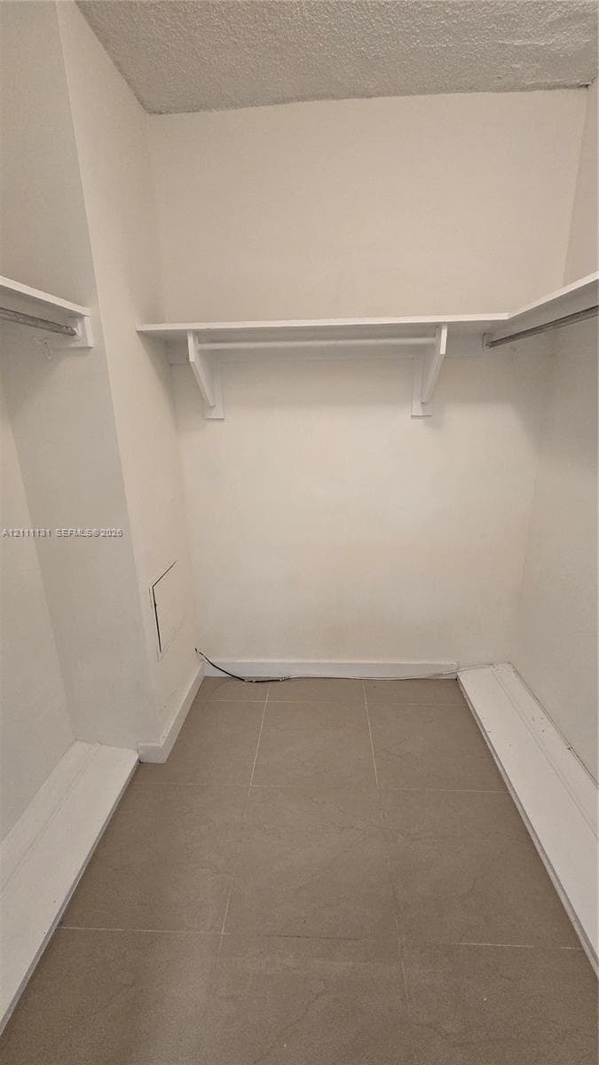 Walk-in storage space featuring neutral tile flooring and multiple built-in shelving and hanging rods