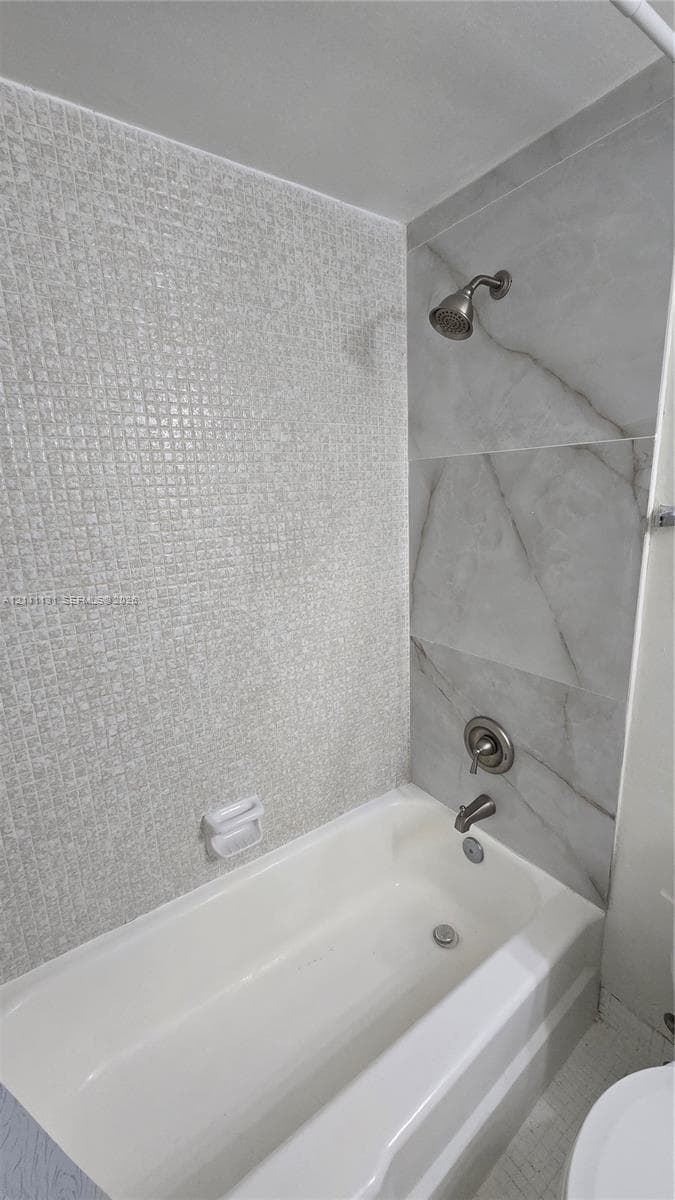 Bathtub with integrated shower, featuring textured mosaic tile accent wall, large-format stone-pattern wall tile, and metallic hardware