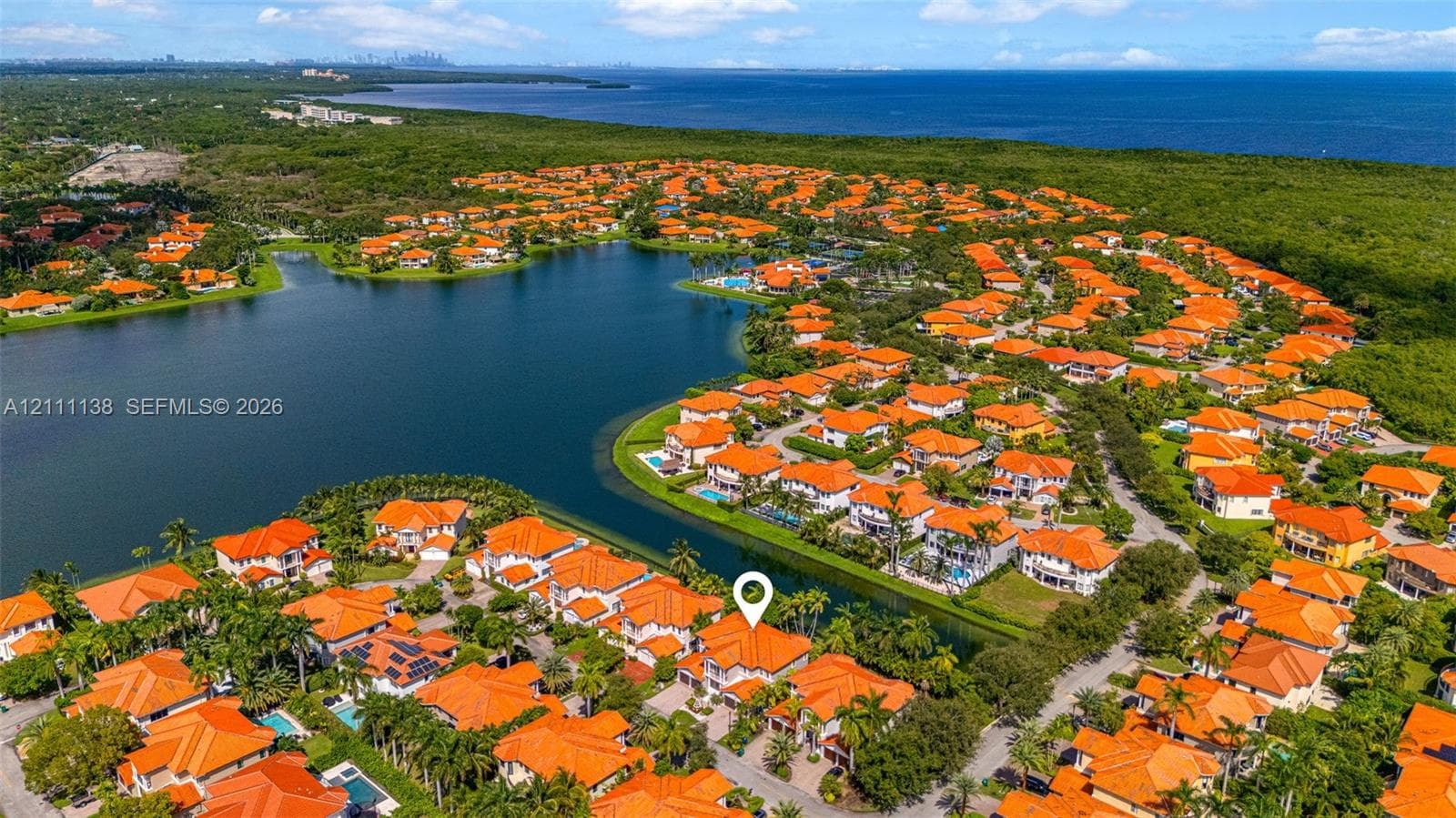 Aerial perspective of a multi-story residence with a tile roof situated in a waterfront community featuring extensive lake frontage and mature palm trees