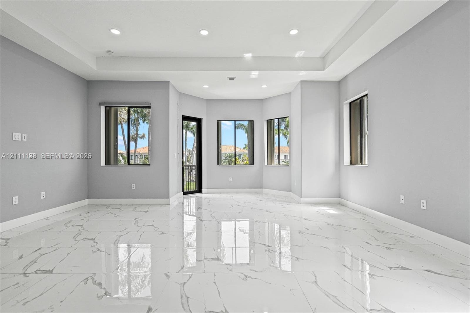 Living space featuring large-format tile flooring with a veined pattern, tray ceiling with recessed lighting, and multiple windows