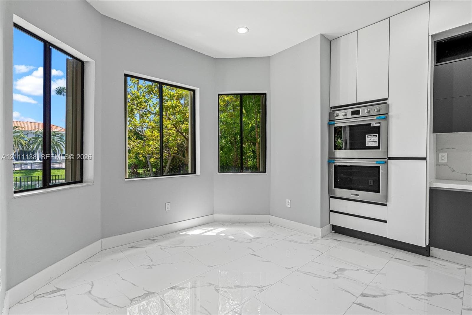 Large-format tile flooring with veining, bay windows, built-in stainless steel double wall oven, and sleek floor-to-ceiling cabinetry