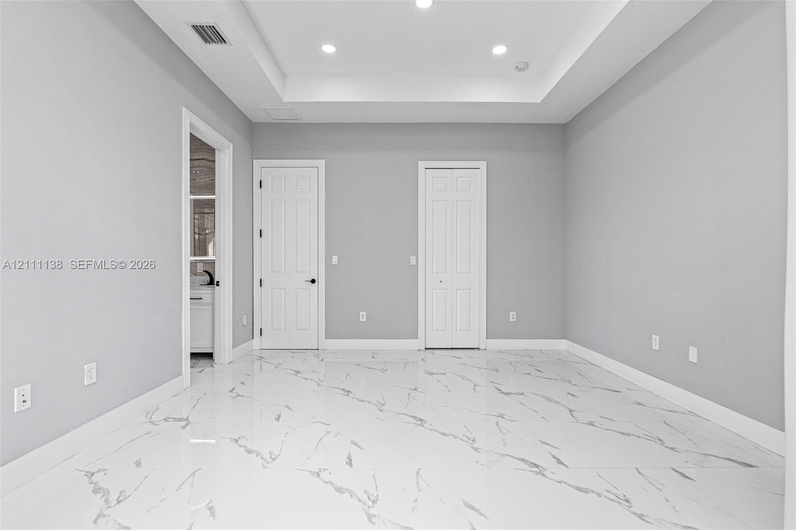 Interior space featuring a recessed tray ceiling, large-format stone-patterned tile flooring, and integrated recessed lighting