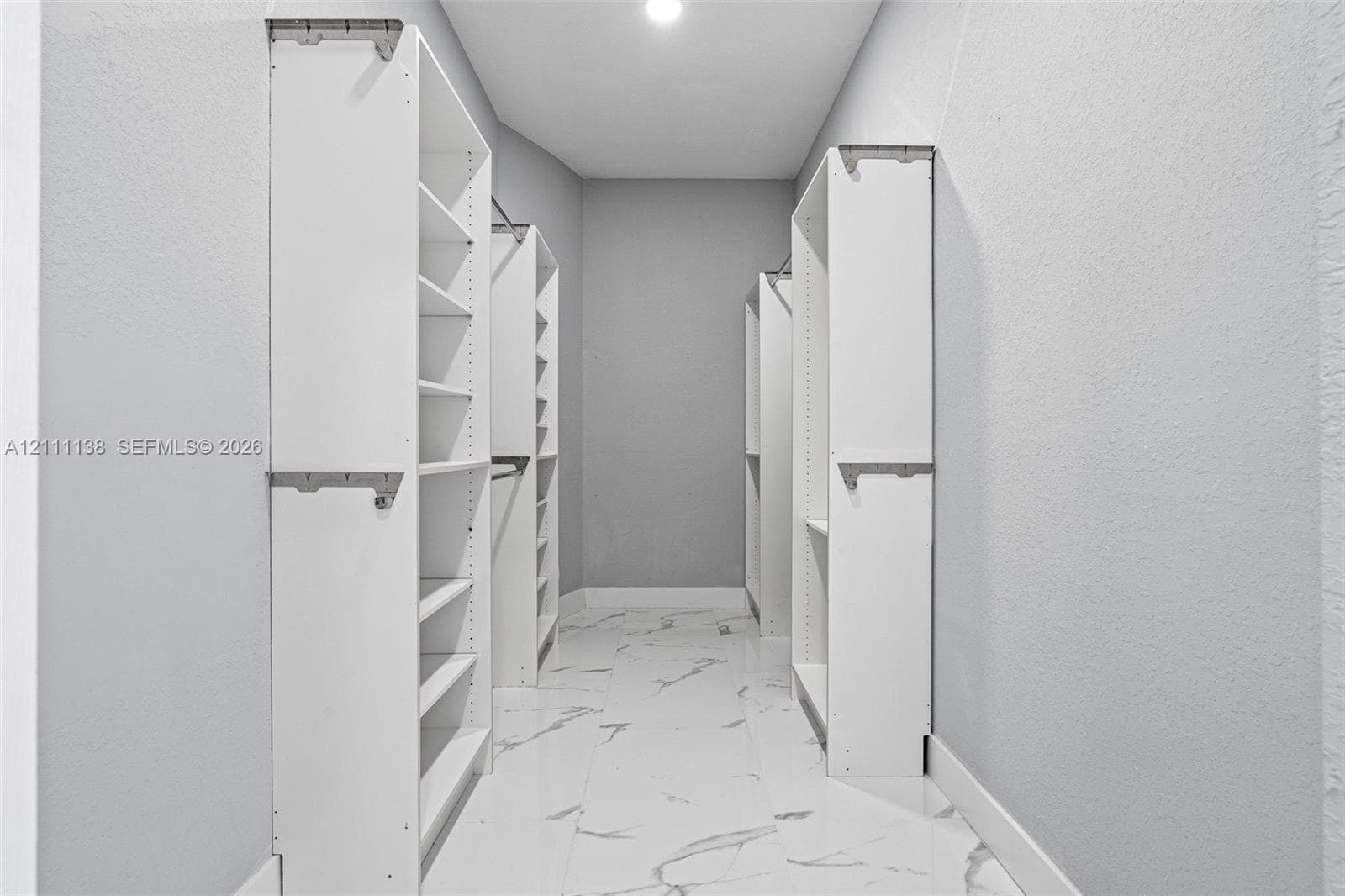 Walk-in closet featuring white built-in shelving, multiple hanging rods, and large-format tile flooring with a neutral vein pattern