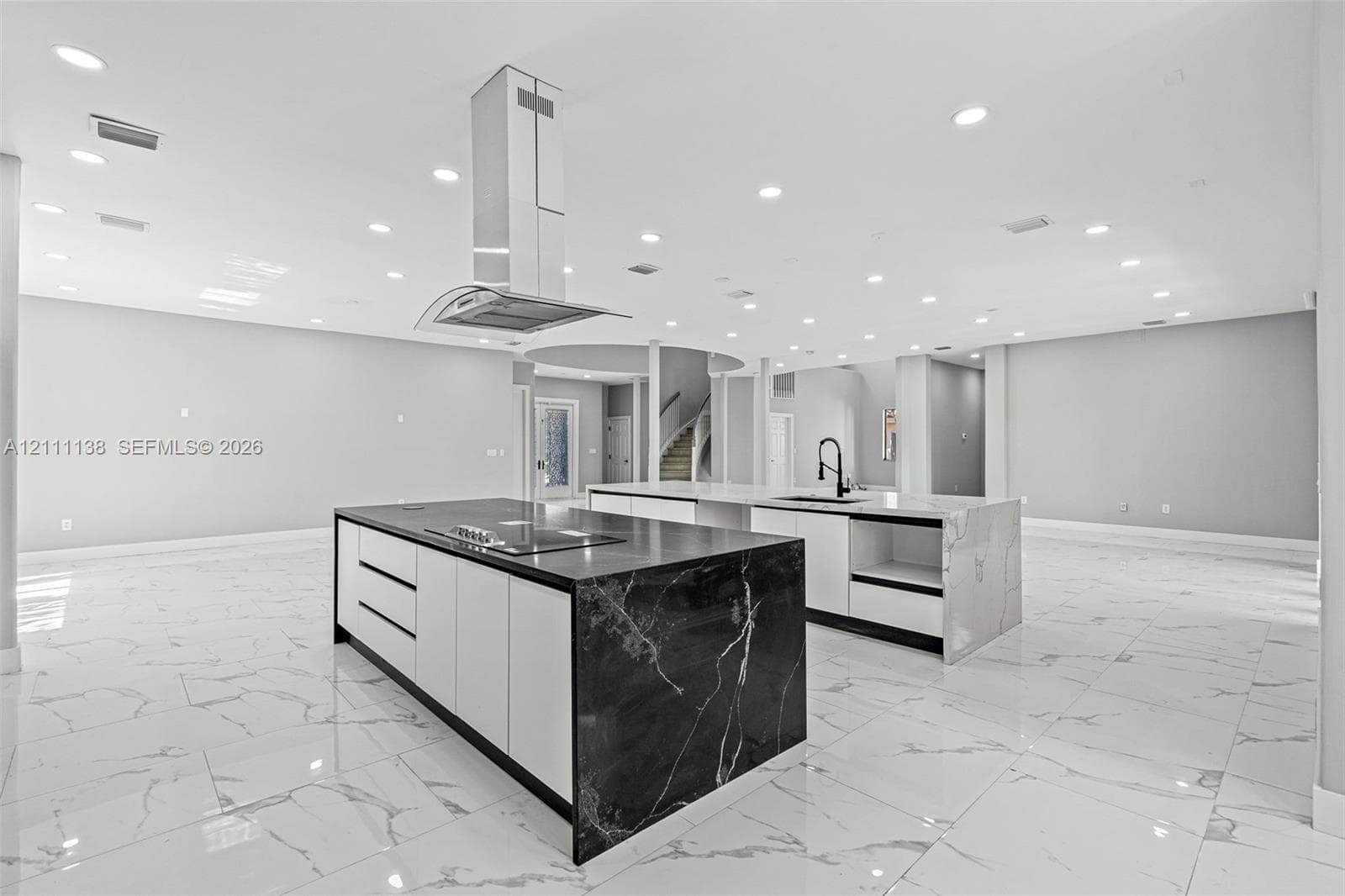 Dual kitchen islands featuring stone-finish waterfall countertops, flat-panel cabinetry, a stainless steel chimney-style range hood, and porcelain tile flooring throughout