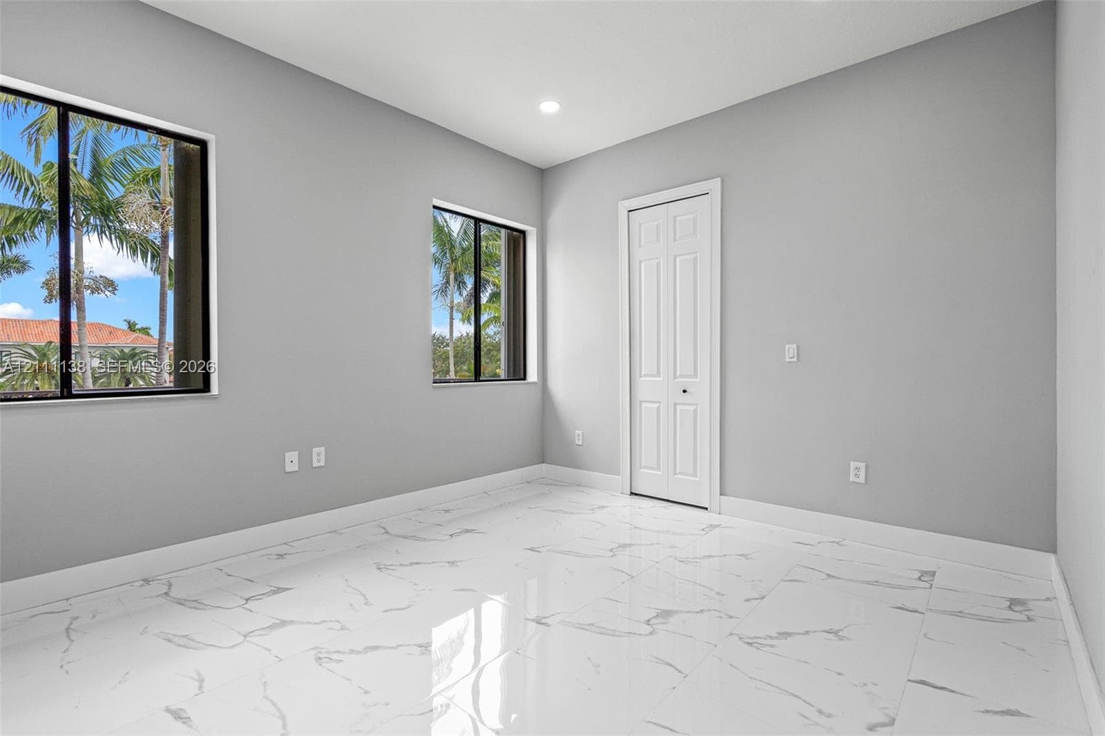 Interior room featuring large-format stone-look flooring, neutral grey walls, dual windows with dark frames, and a white bifold closet door