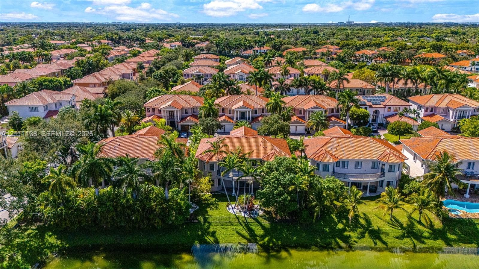 Aerial perspective featuring tile-roofed residences, landscaped grounds with mature palm trees, and waterfront perimeter