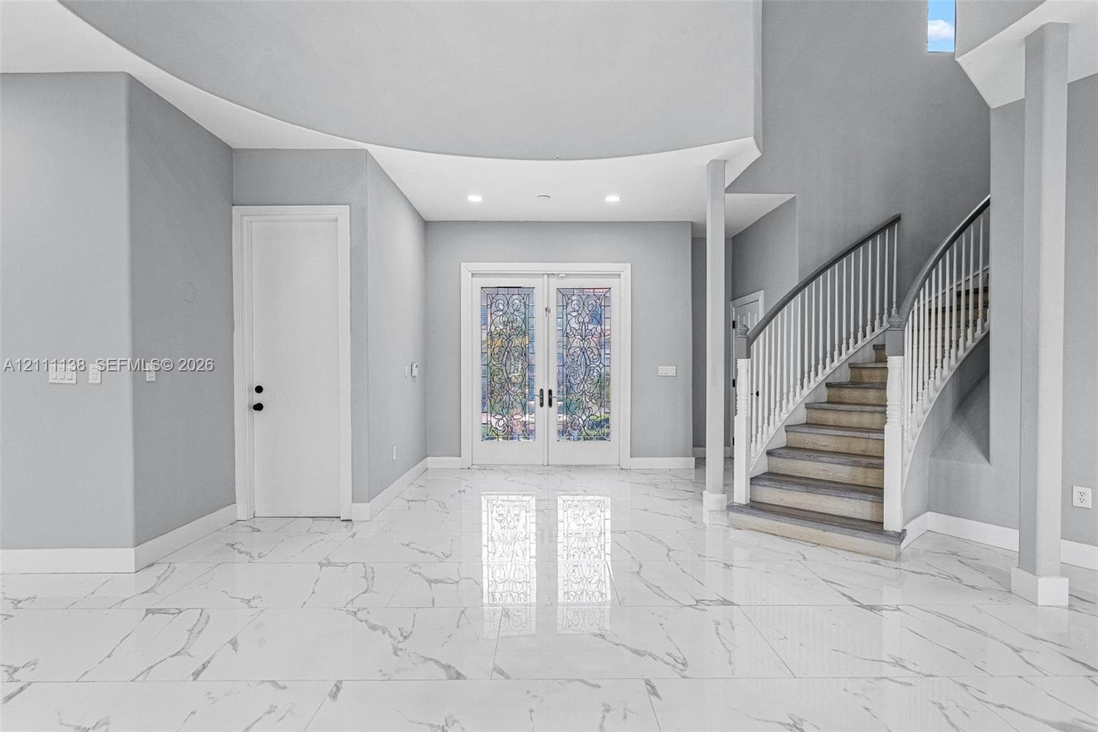 Foyer featuring large-format veined tile flooring, a curved staircase with white spindles, high ceilings with recessed lighting, and double-entry doors