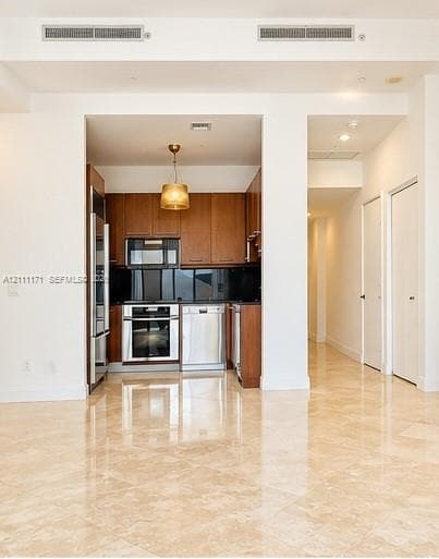 Kitchen featuring wood cabinetry, stainless steel appliances, dark stone backsplash, recessed ceiling lighting, and polished stone flooring