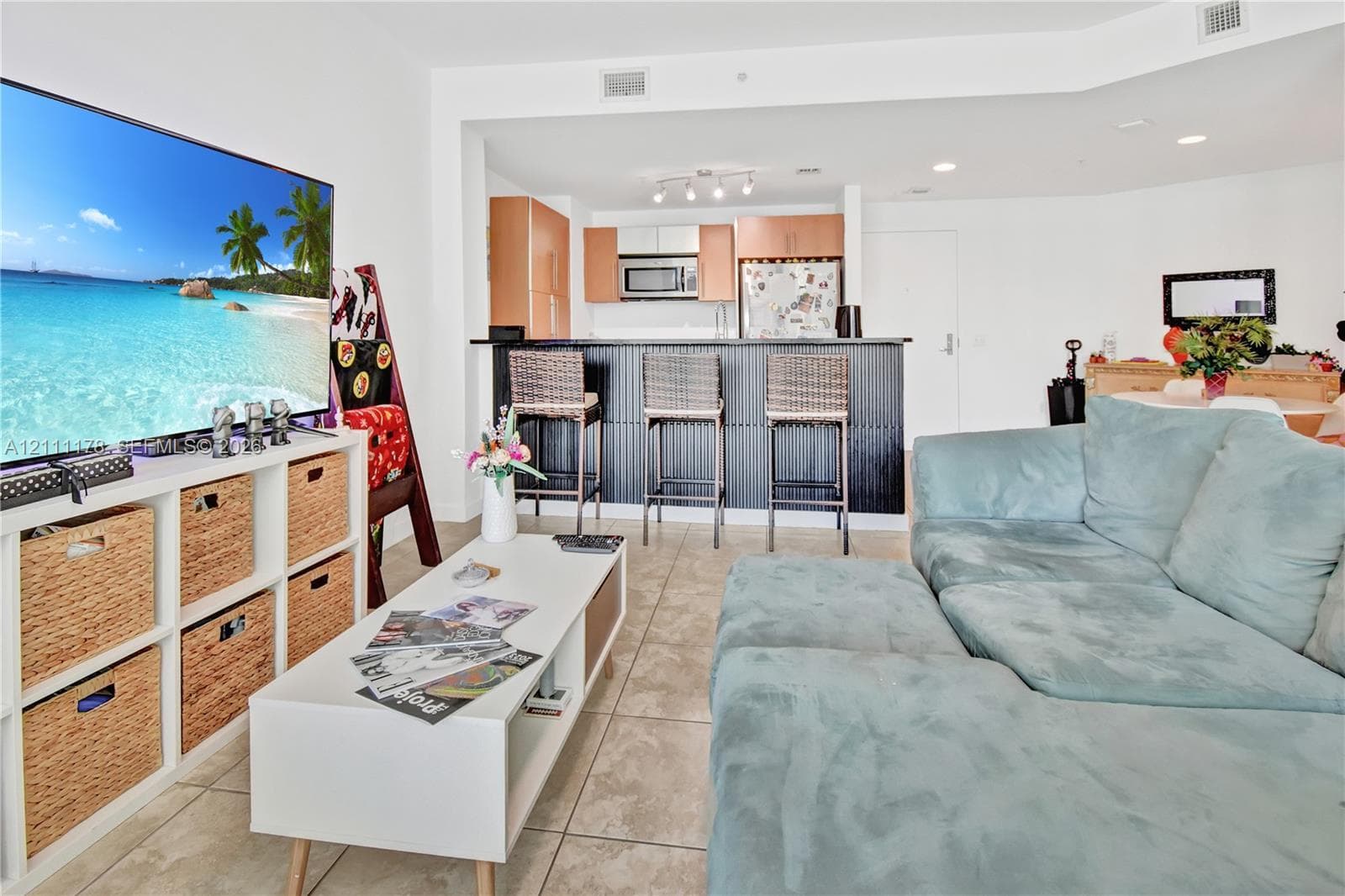 Open-concept area featuring tile flooring, recessed lighting, and a kitchen equipped with wood-finish cabinetry, a microwave, and a black-paneled breakfast bar