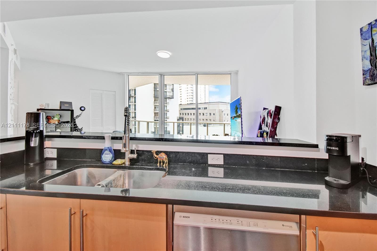 Kitchen featuring dark stone countertops, stainless steel dual-basin sink with pull-down faucet, stainless steel dishwasher, and flat-panel wood cabinetry