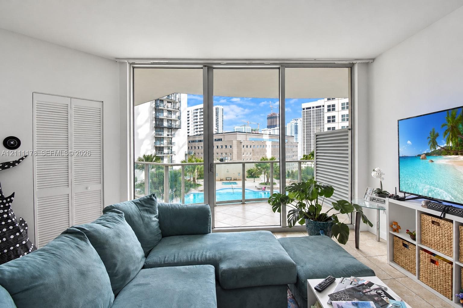 Floor-to-ceiling sliding glass doors, private balcony with metal railing, neutral tile flooring, and louvered double-door closet