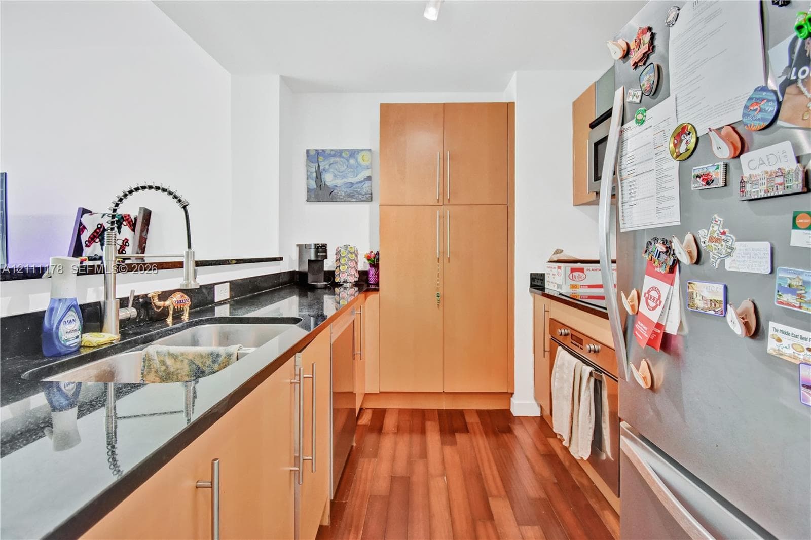 Kitchen featuring light wood-finish cabinetry, dark solid-surface countertops, wood-finish flooring, stainless steel under-mount sink, and commercial-style pull-down faucet