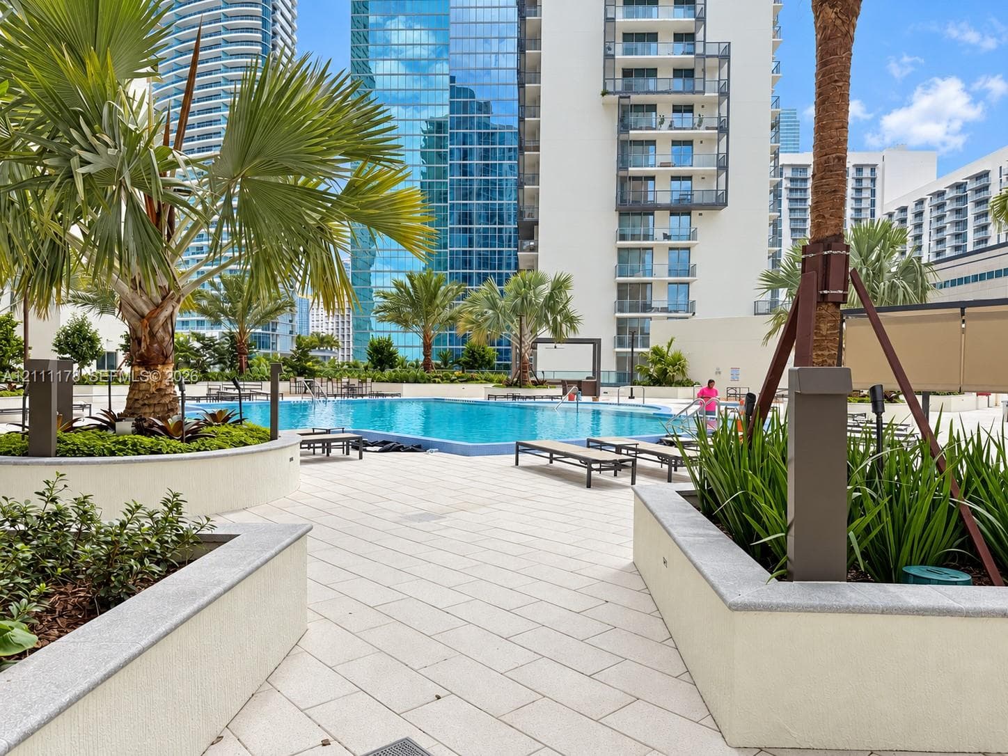 Outdoor pool deck featuring a swimming pool, stone-paver hardscaping, raised concrete planters, and mature palm trees