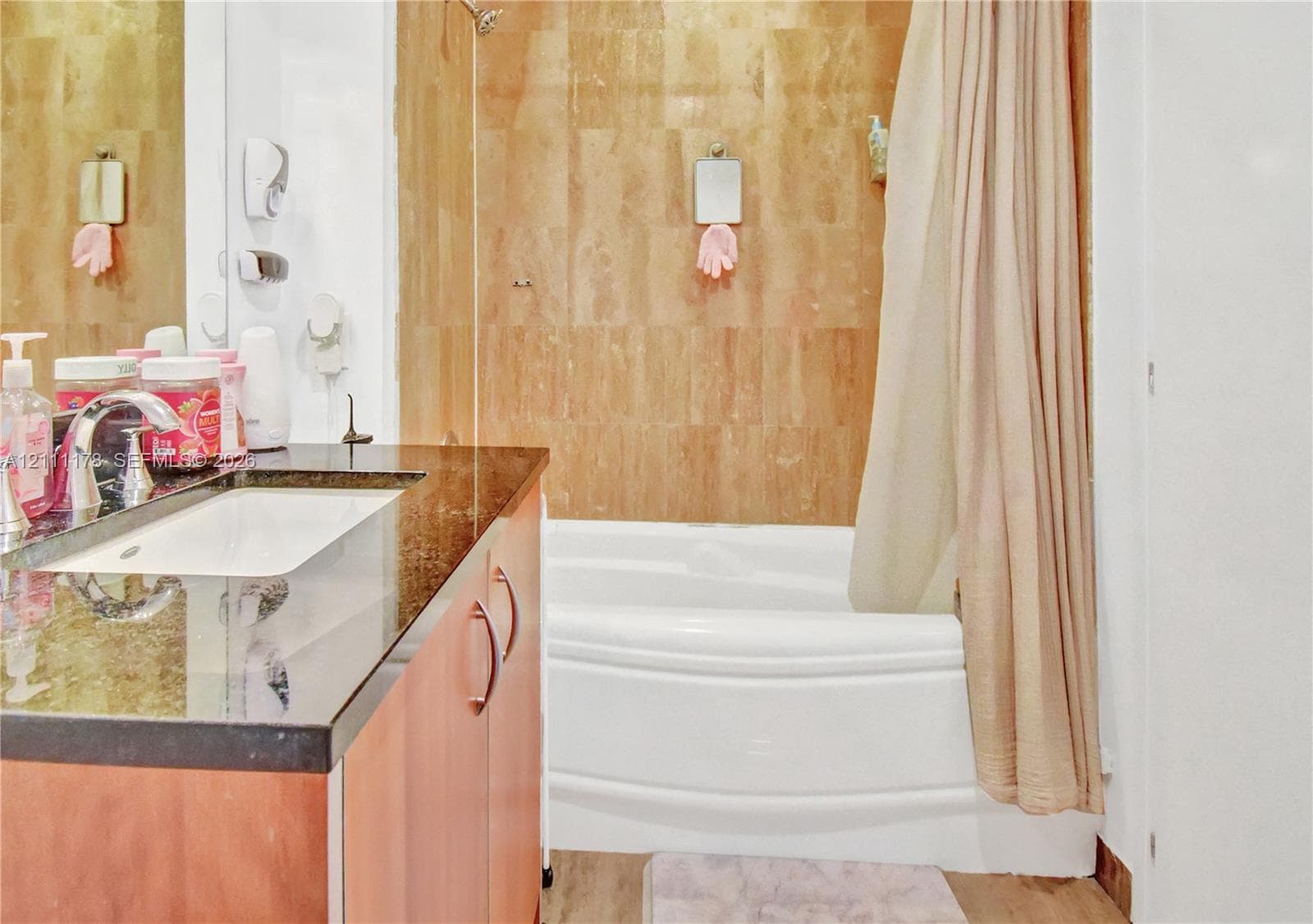 Bathroom featuring a vanity with dark stone countertop, integrated sink, wood-finish cabinetry, and a bathtub with full-height neutral-toned tile surround