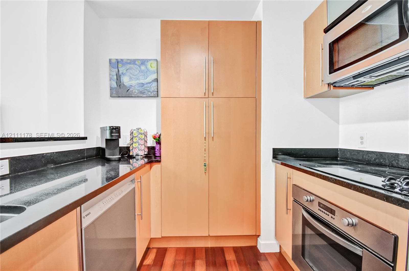 Kitchen featuring light-toned wood cabinetry, dark stone countertops, stainless steel wall oven, stainless steel built-in microwave, and wood-finish flooring