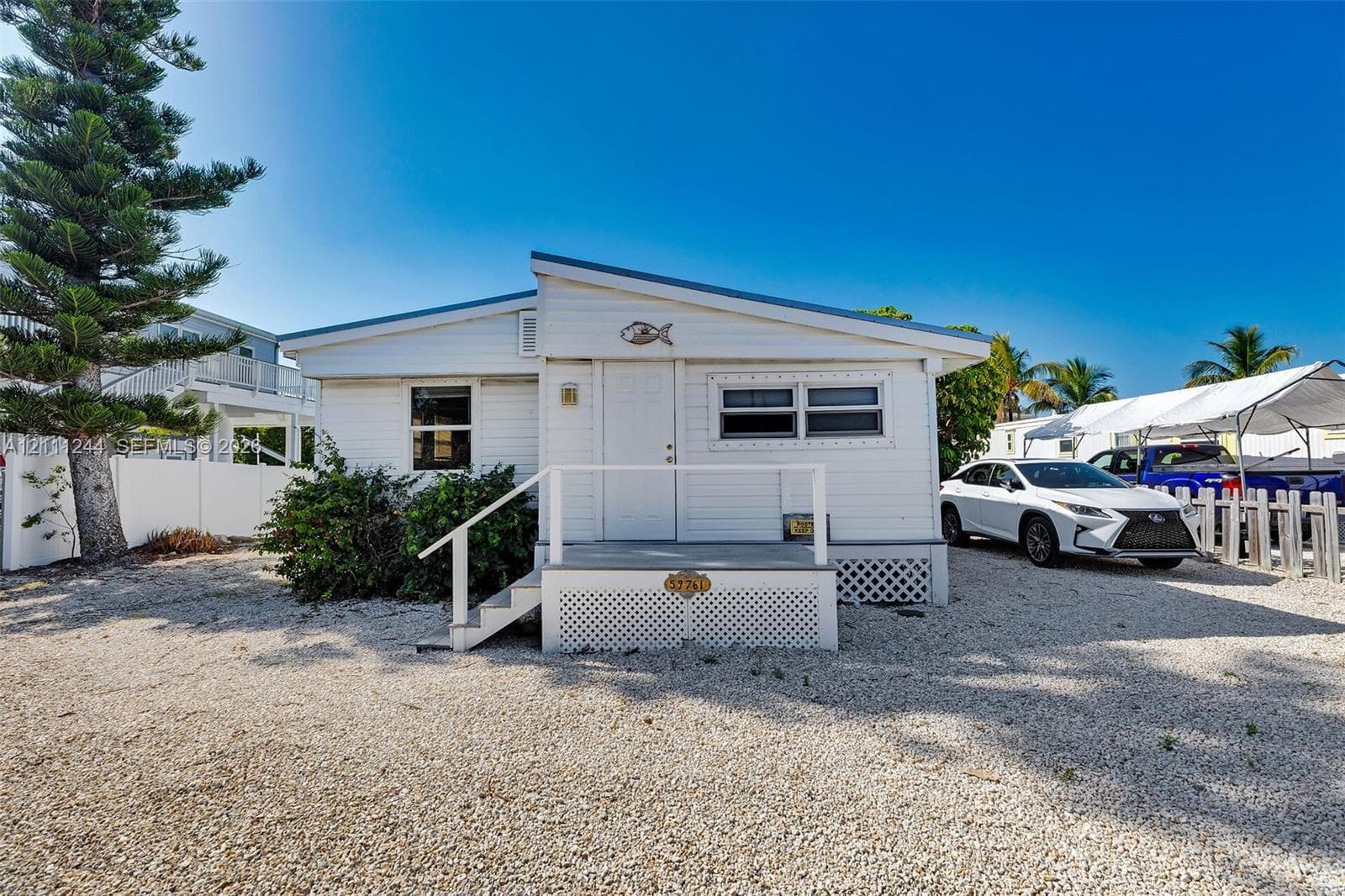 Single-story exterior featuring white horizontal siding, a shed-style roofline, an elevated front entry porch with white railings, and a lattice-skirted foundation