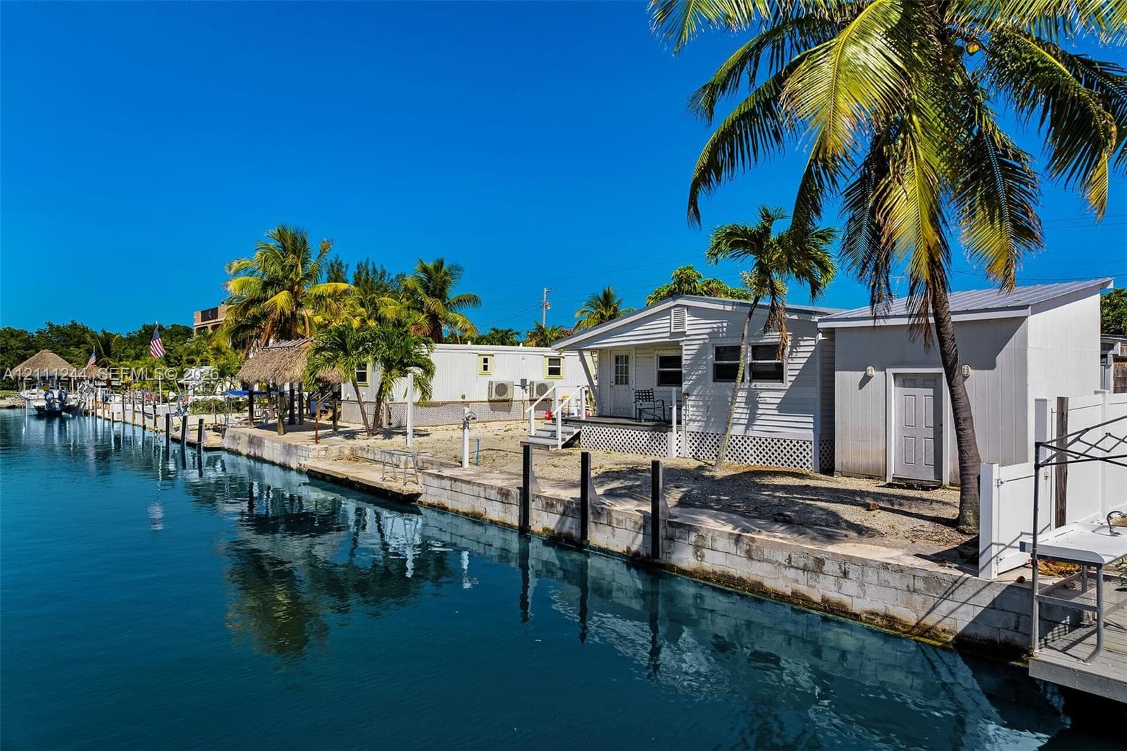 Waterfront property featuring a concrete seawall, private boat slip, thatched-roof cabana, and mature palm trees