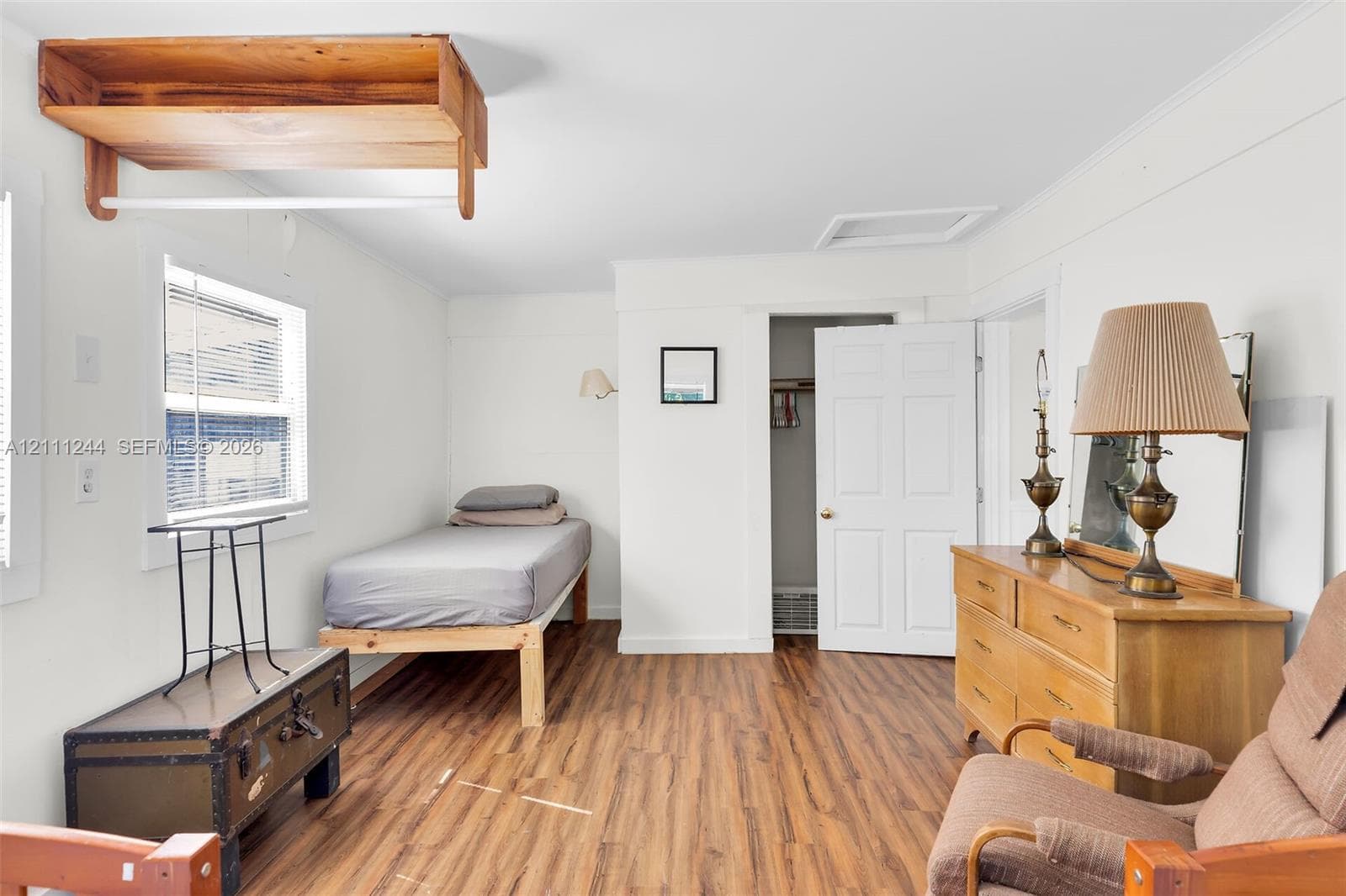 Room featuring wood-finish flooring, a wall-mounted wooden shelf, and a multi-panel interior door