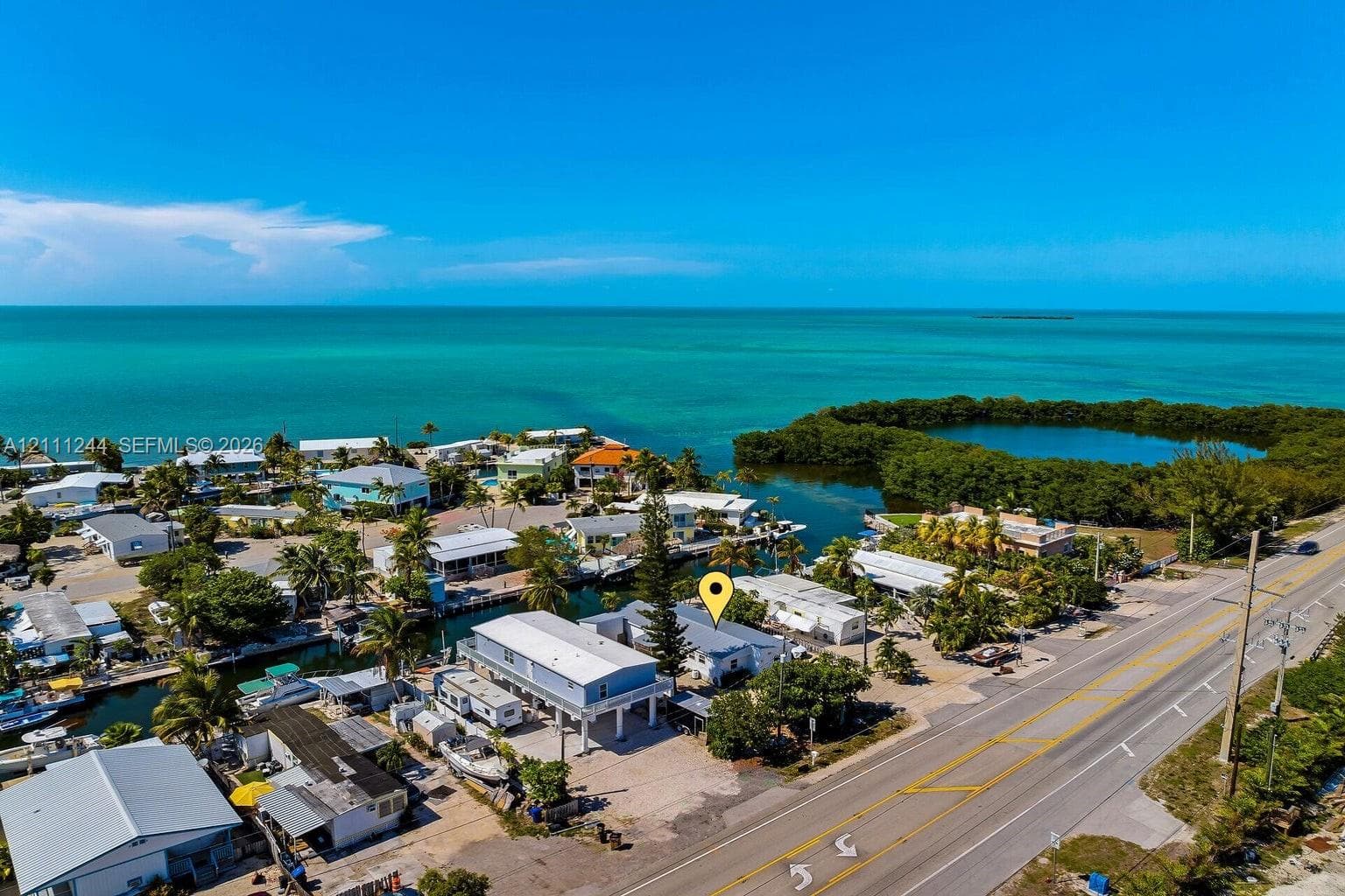 Aerial perspective of a coastal property featuring waterfront access, elevated structural design, gravel lot, and proximity to open water