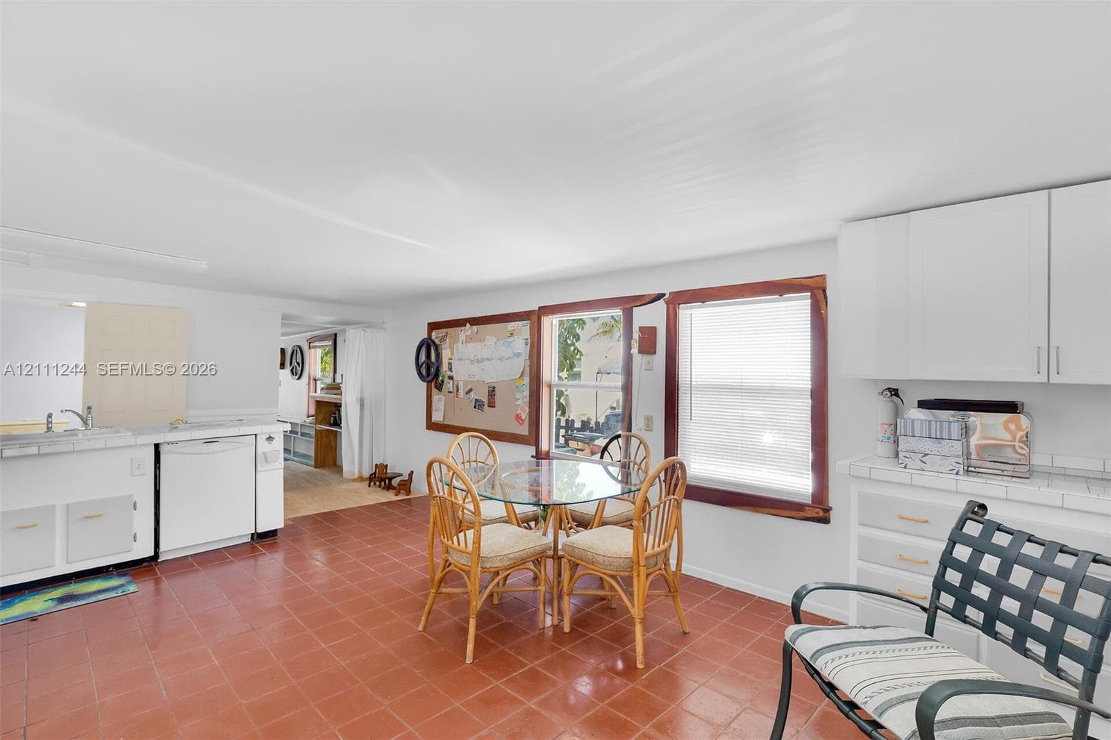 Kitchen space featuring tile flooring, white cabinetry with tile countertops, integrated dishwasher, and wood-trimmed windows