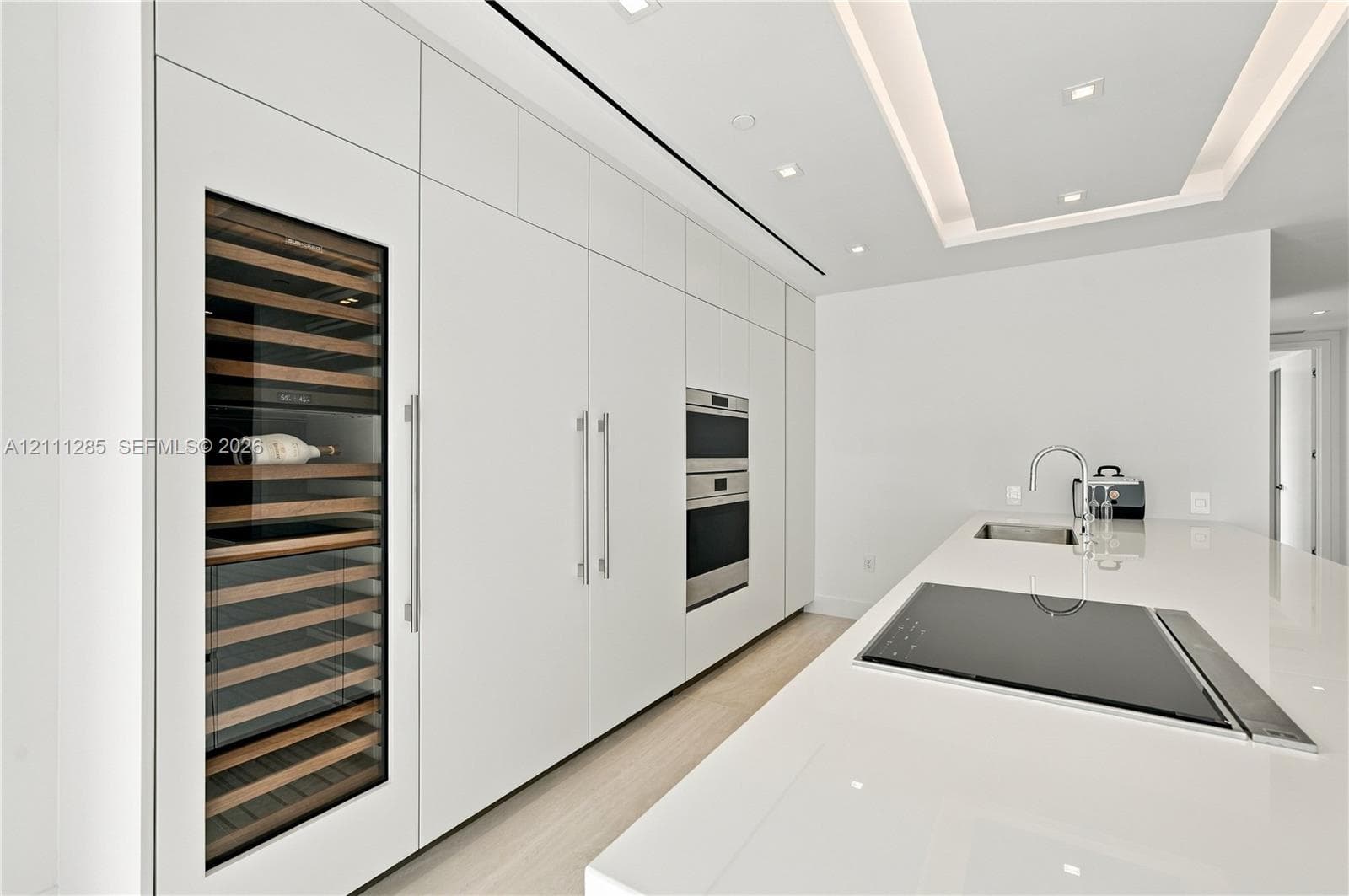 Sleek kitchen featuring custom floor-to-ceiling cabinetry, built-in stainless steel appliances, a glass-front wine refrigerator, and a solid-surface island with an integrated cooktop and undermount sink