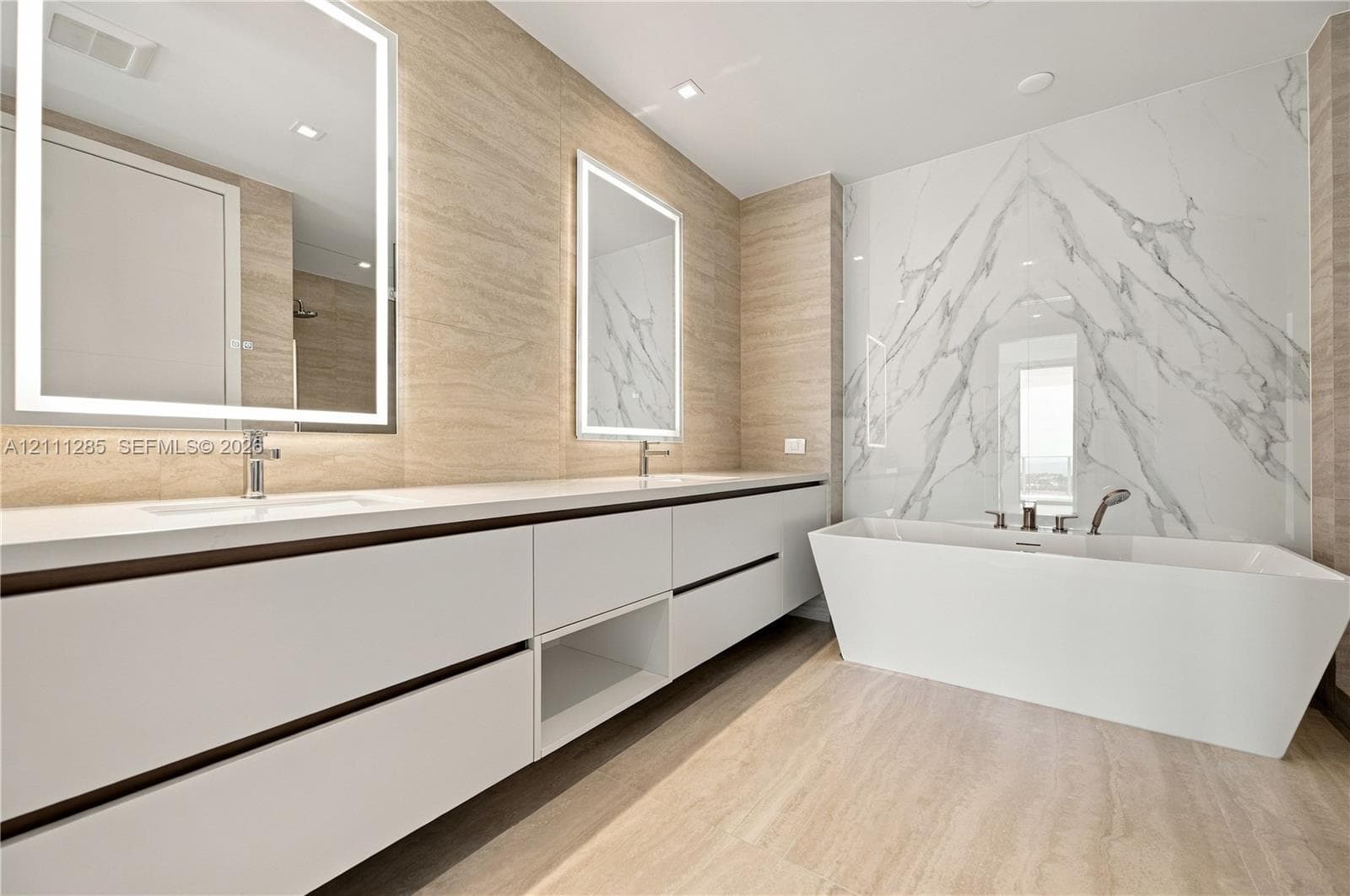 Dual-sink vanity with white cabinetry and countertop, backlit rectangular mirrors, freestanding soaking tub, and large-format tile surround