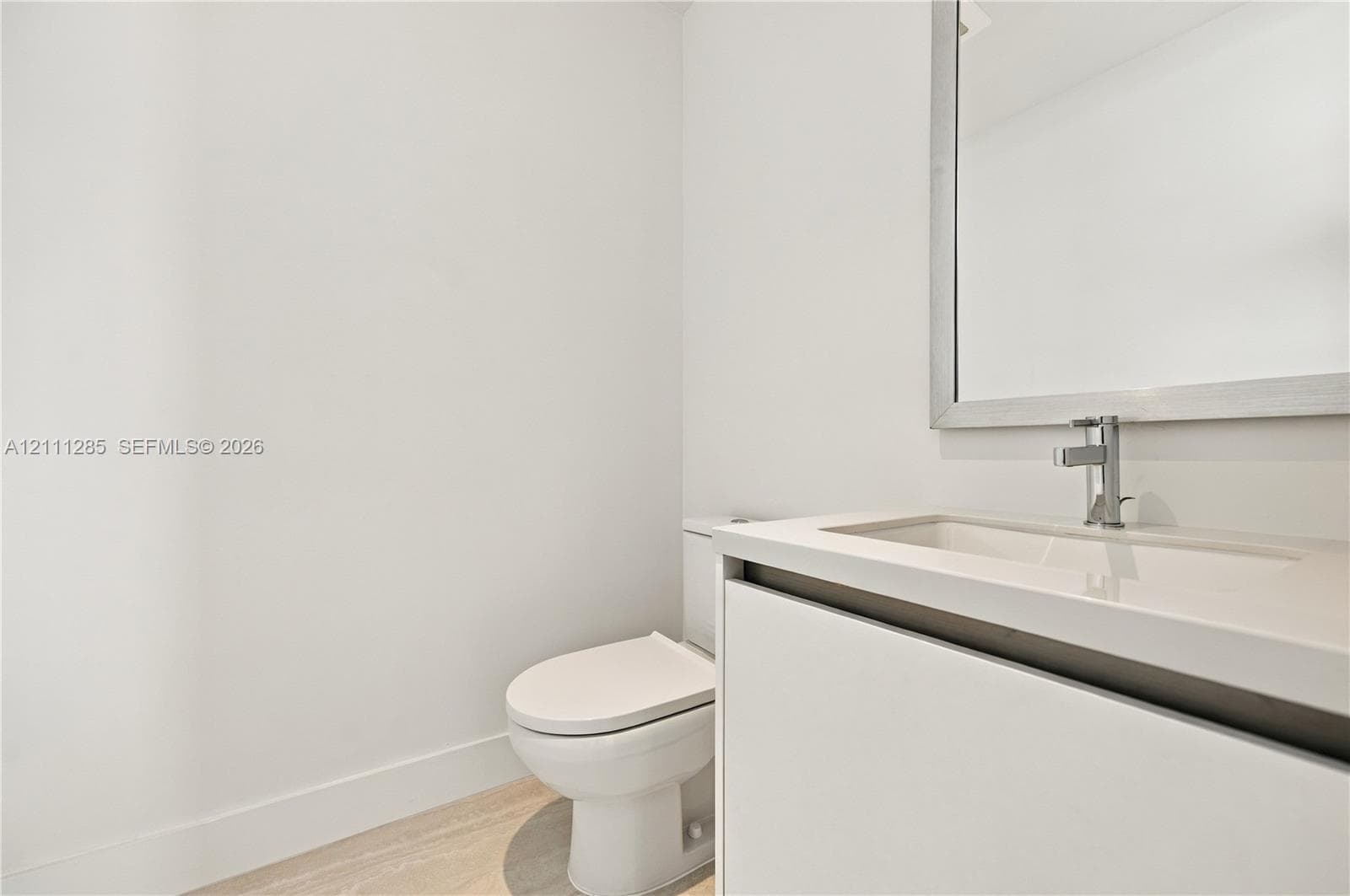 Modern vanity featuring a seamless integrated countertop and sink, wall-mounted mirror with a metallic frame, chrome faucet, and light-toned wood-finish flooring
