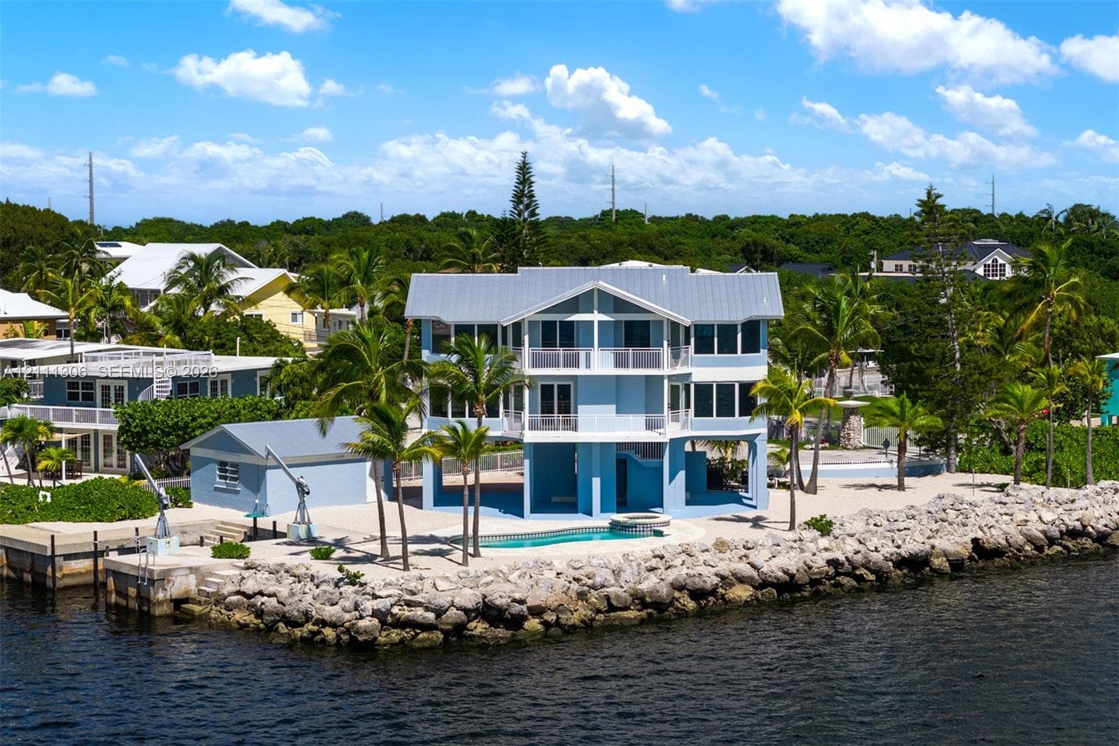 Three-story waterfront residence featuring multi-level covered balconies, an elevated structural design, a custom-shaped swimming pool, and a private dock with mechanical boat lift
