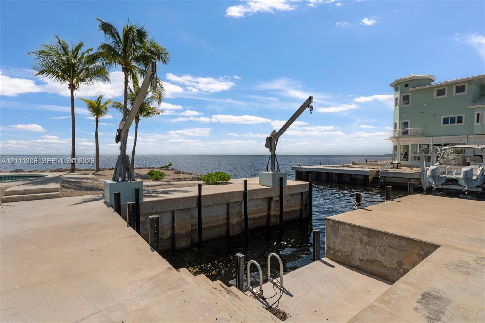 Waterfront concrete dock featuring dual boat lifts, integrated swimming ladder, and expansive open-water frontage