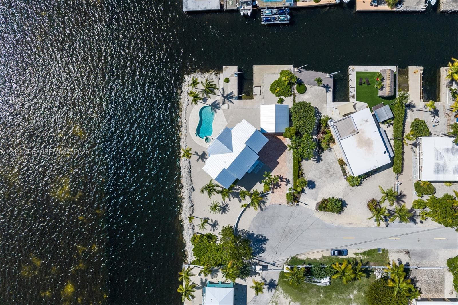 Waterfront property featuring a private boat dock, in-ground swimming pool, paved driveway, and mature palm trees