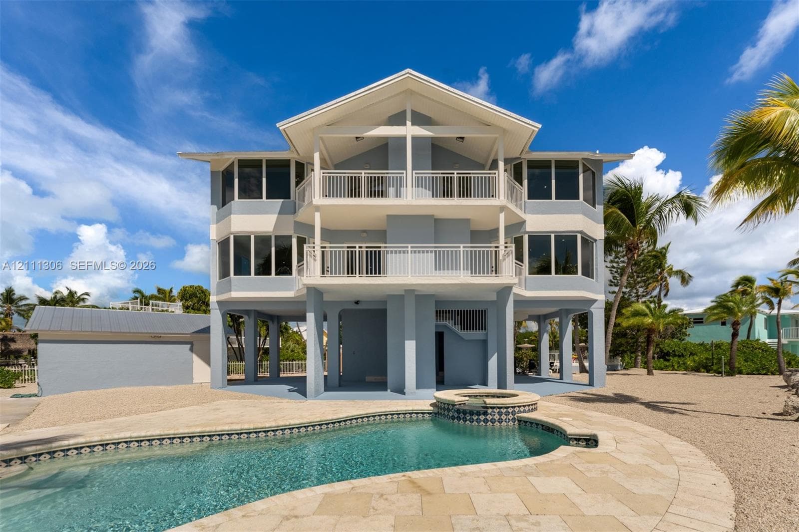Three-story stilt structure featuring multi-level covered balconies, an inground swimming pool with integrated spa, stone-paver pool deck, and a detached garage