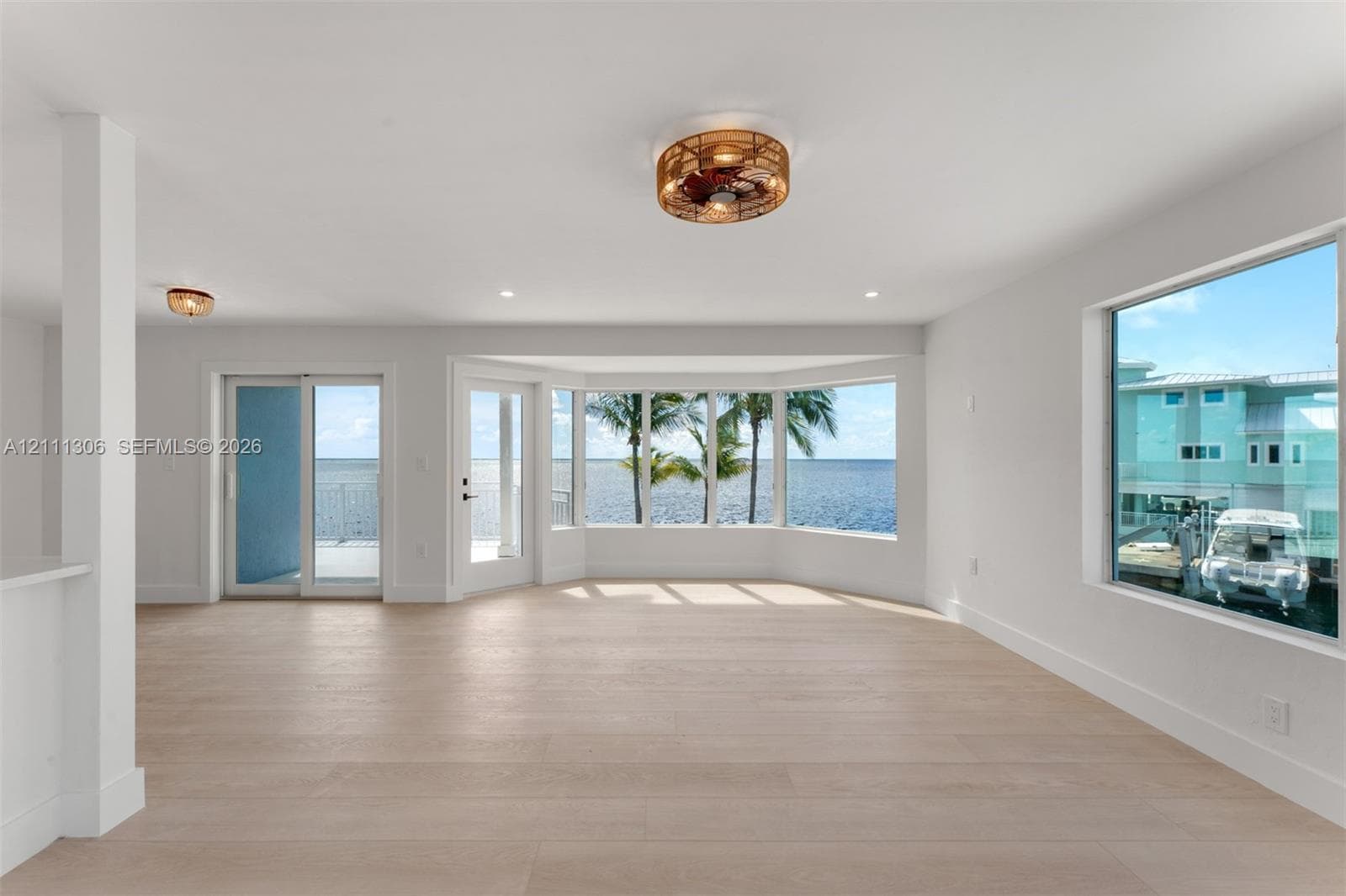 Open-concept space featuring light-toned wood-finish flooring, a bay window, sliding glass doors, and drum-style ceiling light fixtures