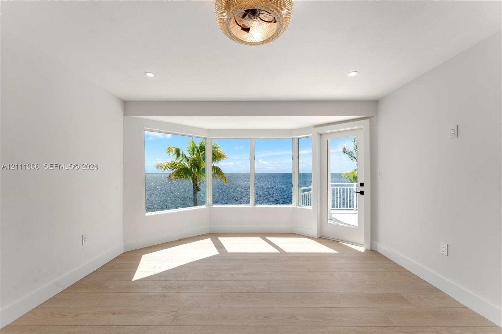 Bay window with water backdrop, wood-finish flooring, recessed lighting, woven-texture ceiling fixture, and glass-paneled exterior door