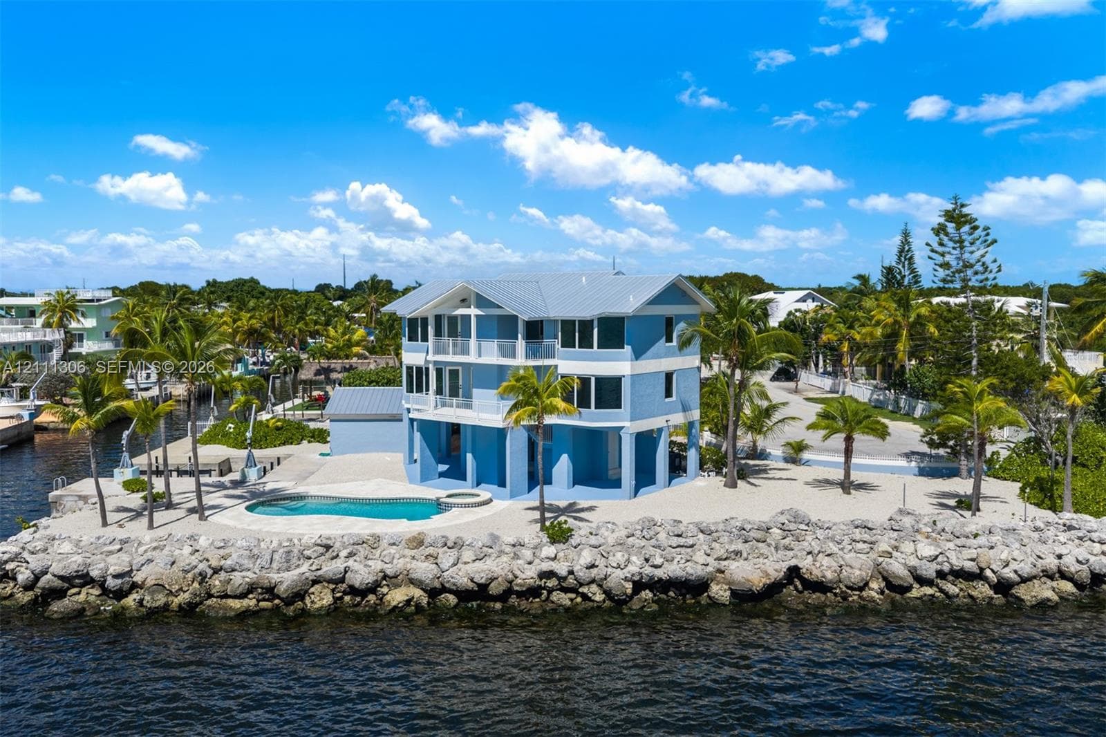 Multi-level coastal residence featuring metal roofing, private swimming pool with integrated spa, concrete sea wall, and expansive open-air balconies