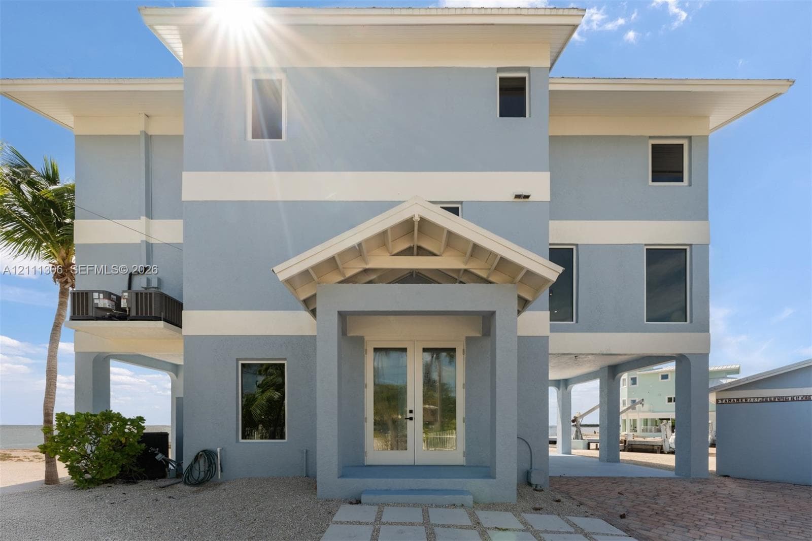 Multi-story coastal residence featuring a stilt-foundation design, stucco exterior, gabled entryway, double-door main entrance, and stone-paver walkway