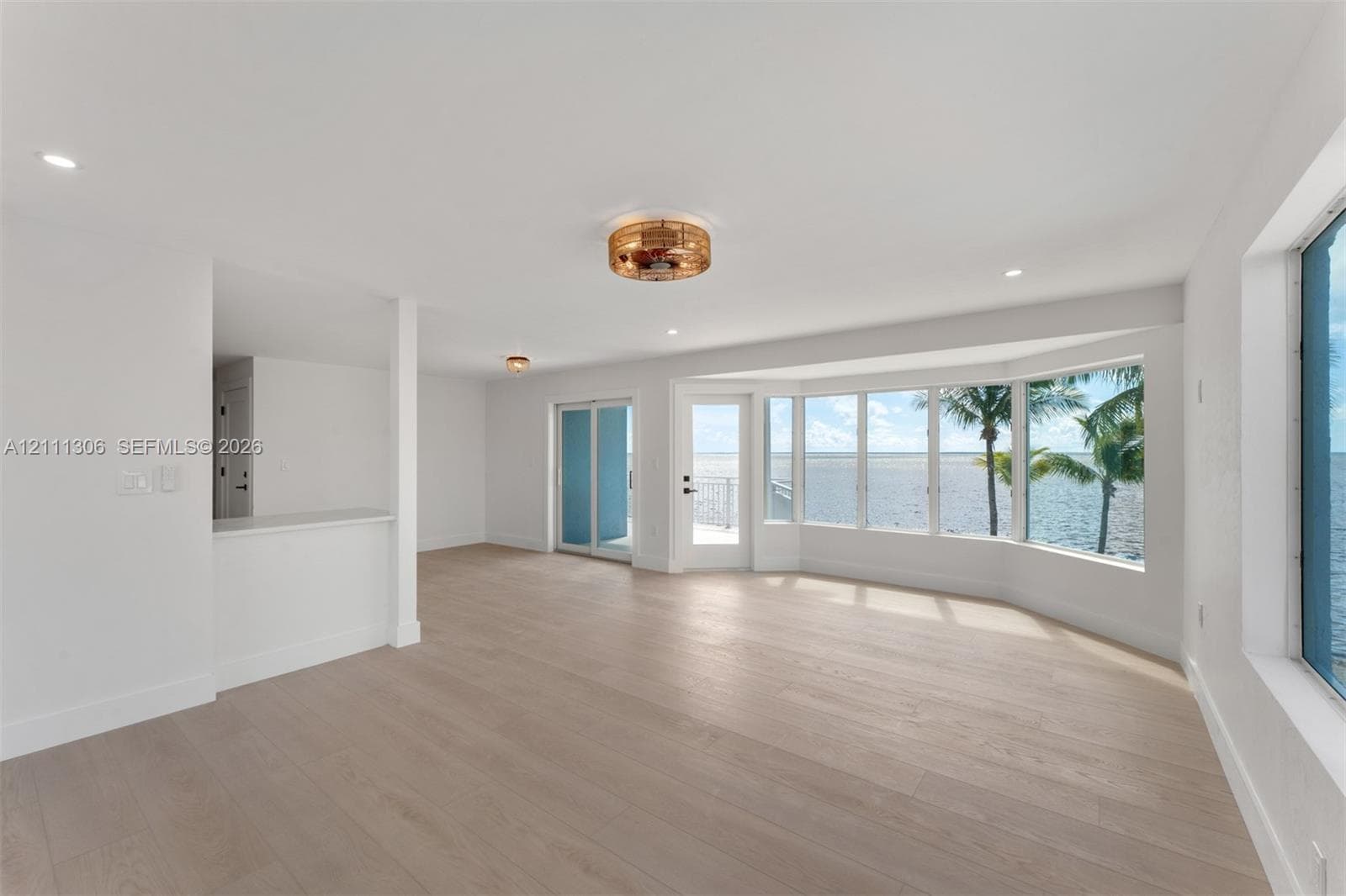 Open-concept interior featuring light-toned wood-finish flooring, a bay window with water frontage, recessed lighting, and a glass-paneled exterior door