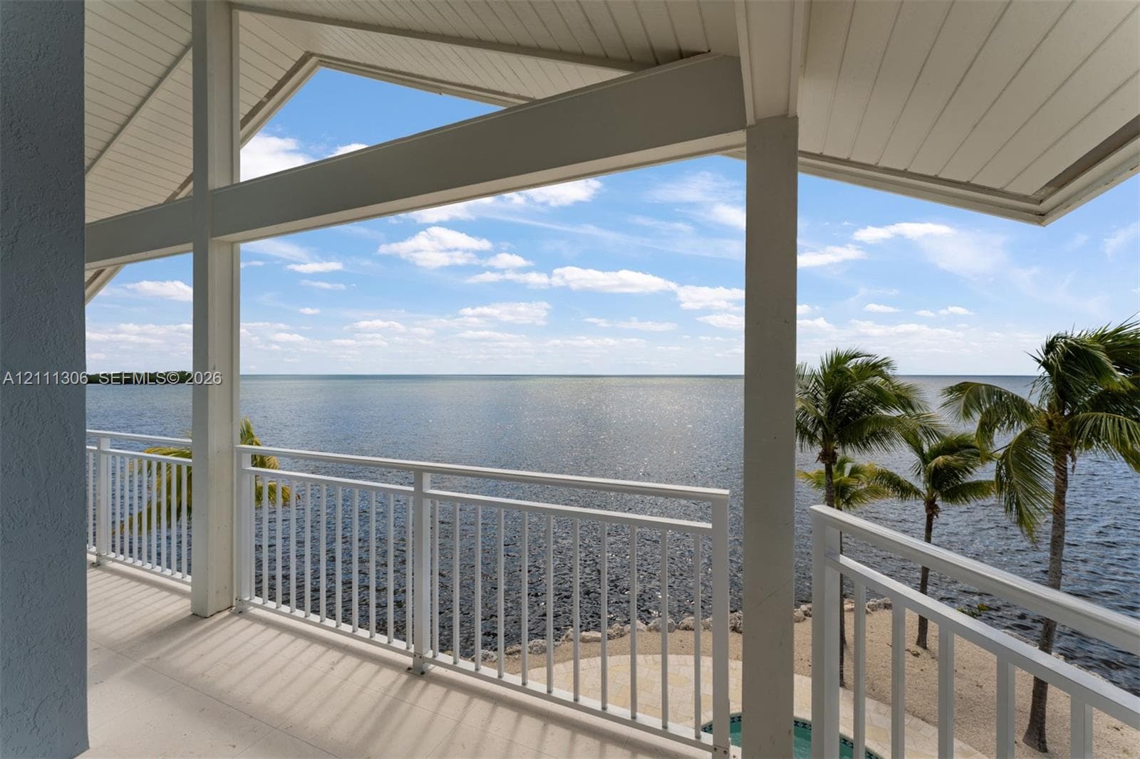 Covered balcony featuring vaulted tongue-and-groove ceiling, white metal railings, and concrete flooring overlooking the water